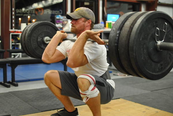 man front squatting a large weight with a barbell